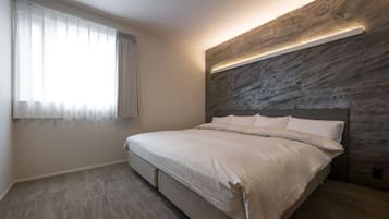 A bedroom with a bed, a window with curtains, a wall with a textured pattern, and a ceiling vent.