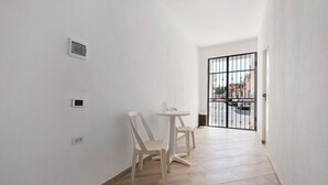 A narrow hallway with white walls, a small table with chairs, and a barred gate leading outside.
