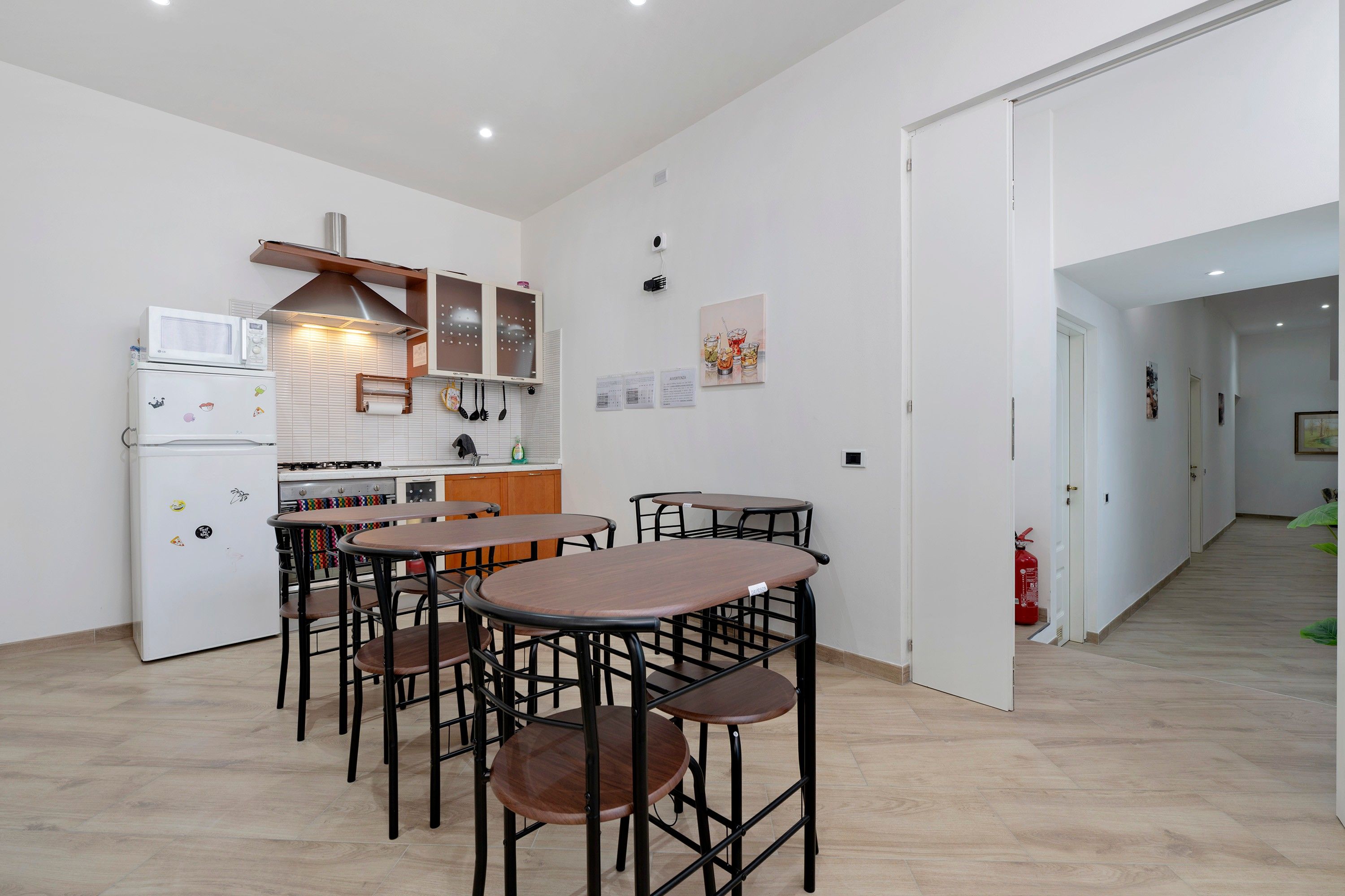 A compact kitchen with modern appliances, a dining area with four stools, and a hallway leading to another room.
