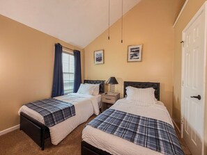 Un dormitorio con dos camas, una ventana con cortinas, una mesita de noche con lámpara y una puerta.