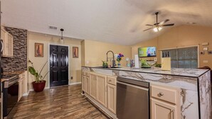 A kitchen with wooden flooring, a marble countertop, a dishwasher, a ceiling fan, and a TV mounted on the wall. - 3BR Atlanta Airport Home | Pet Friendly + Parking (Union City)