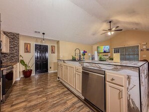 A kitchen with wooden flooring, a marble countertop, a dishwasher, a ceiling fan, and a TV mounted on the wall. - 3BR Atlanta Airport Home | Pet Friendly + Parking (Union City)