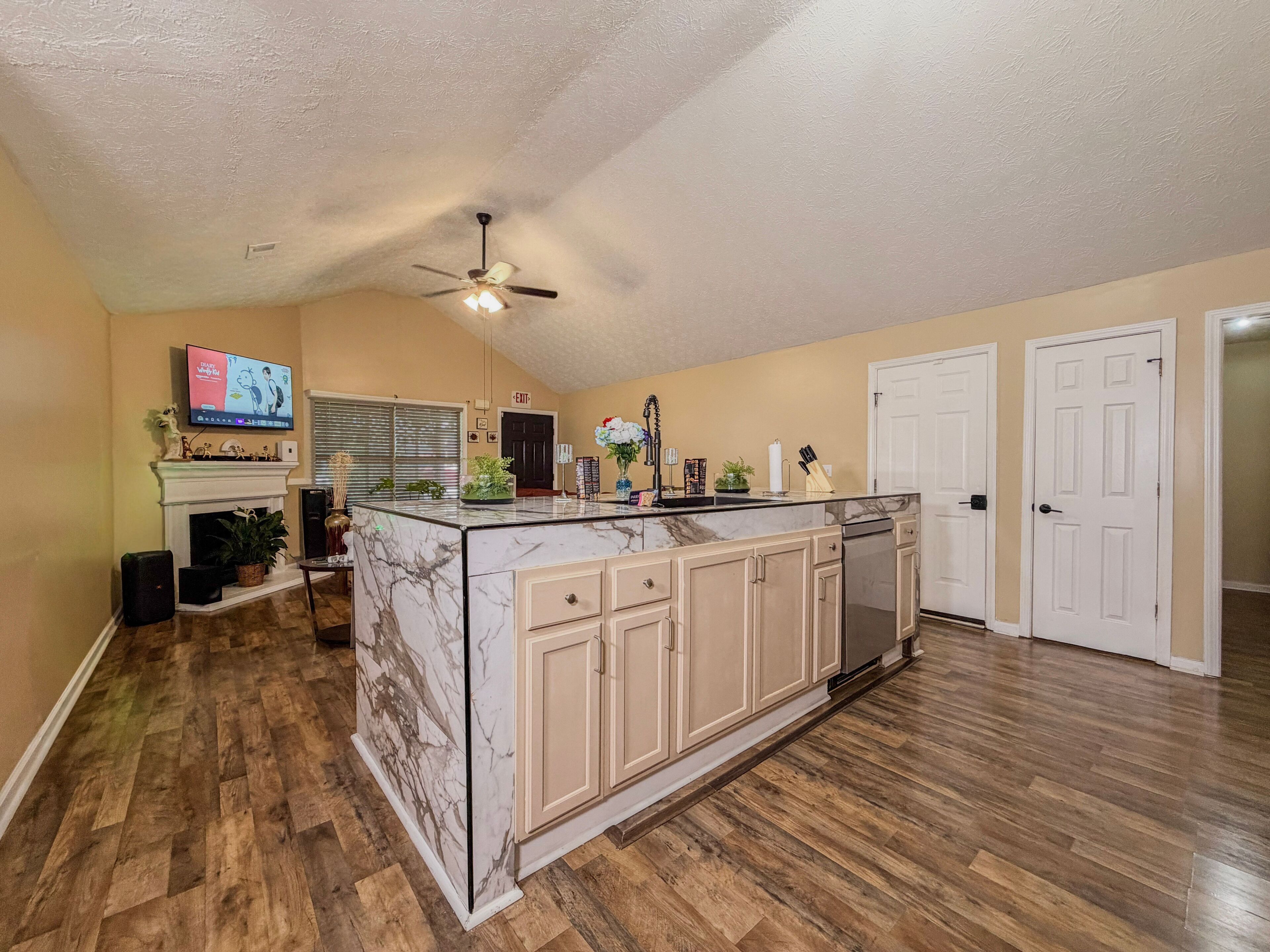 A spacious kitchen with a marble island, wooden flooring, and a ceiling fan.