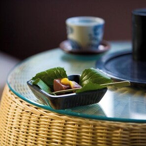 A wicker table with a glass top, a small dish with food and a leaf, and a cup with saucer in the background.