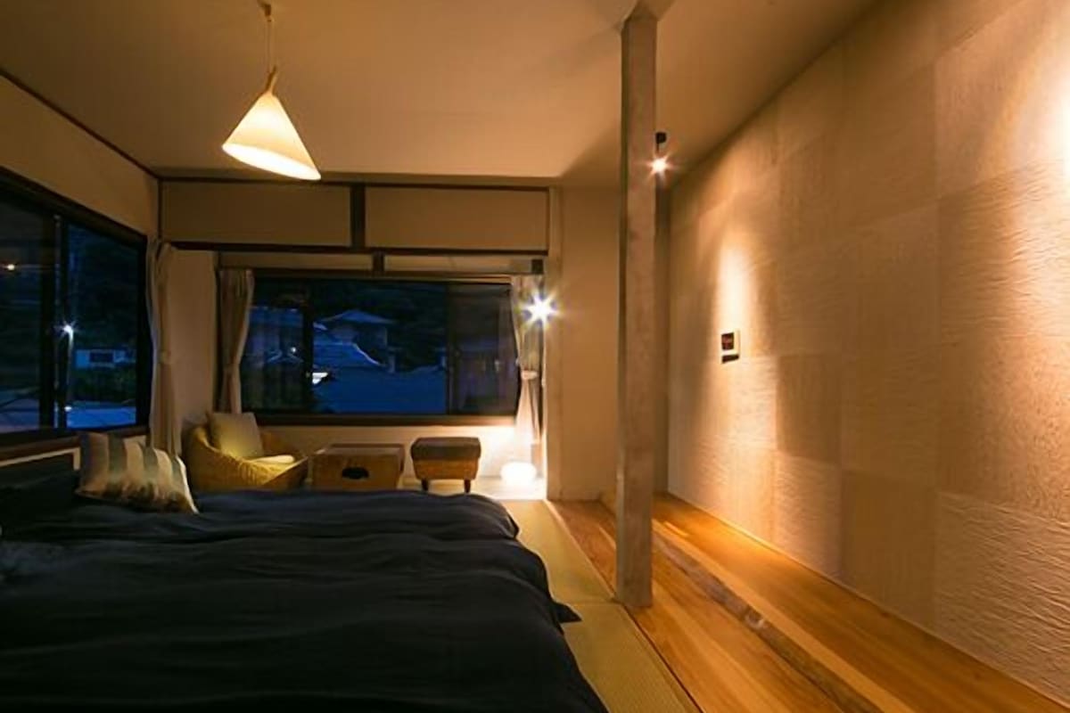 A bedroom with a bed, bedside tables, a window, and a wall-mounted light fixture.