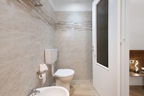 A bathroom with a toilet, bidet, and sink, tiled walls, and a wooden vanity with a mirror.