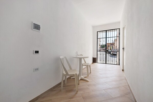 A narrow hallway with white walls, a small table with chairs, and a barred gate leading outside.