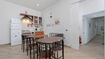 Cozinha compacta com eletrodomésticos modernos, área de refeições com quatro banquetas, e corredor que dá para outro cômodo.