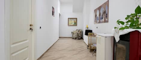 A hallway with a white door, a framed painting, a patterned armchair, and a small table with a plant.