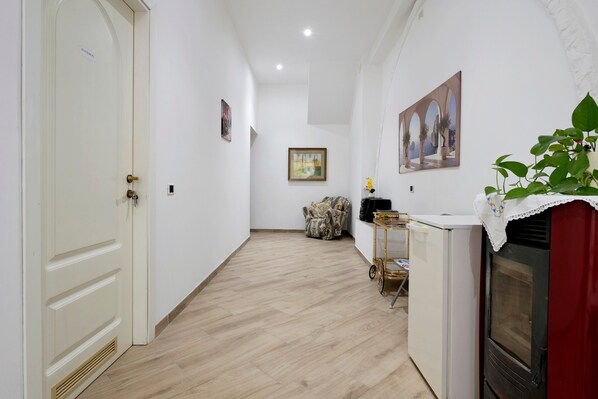 A hallway with a white door, a framed painting, a patterned armchair, and a small table with a plant.