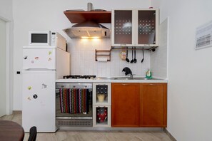 A compact kitchen with a refrigerator, microwave, stove, oven, and wooden cabinets.