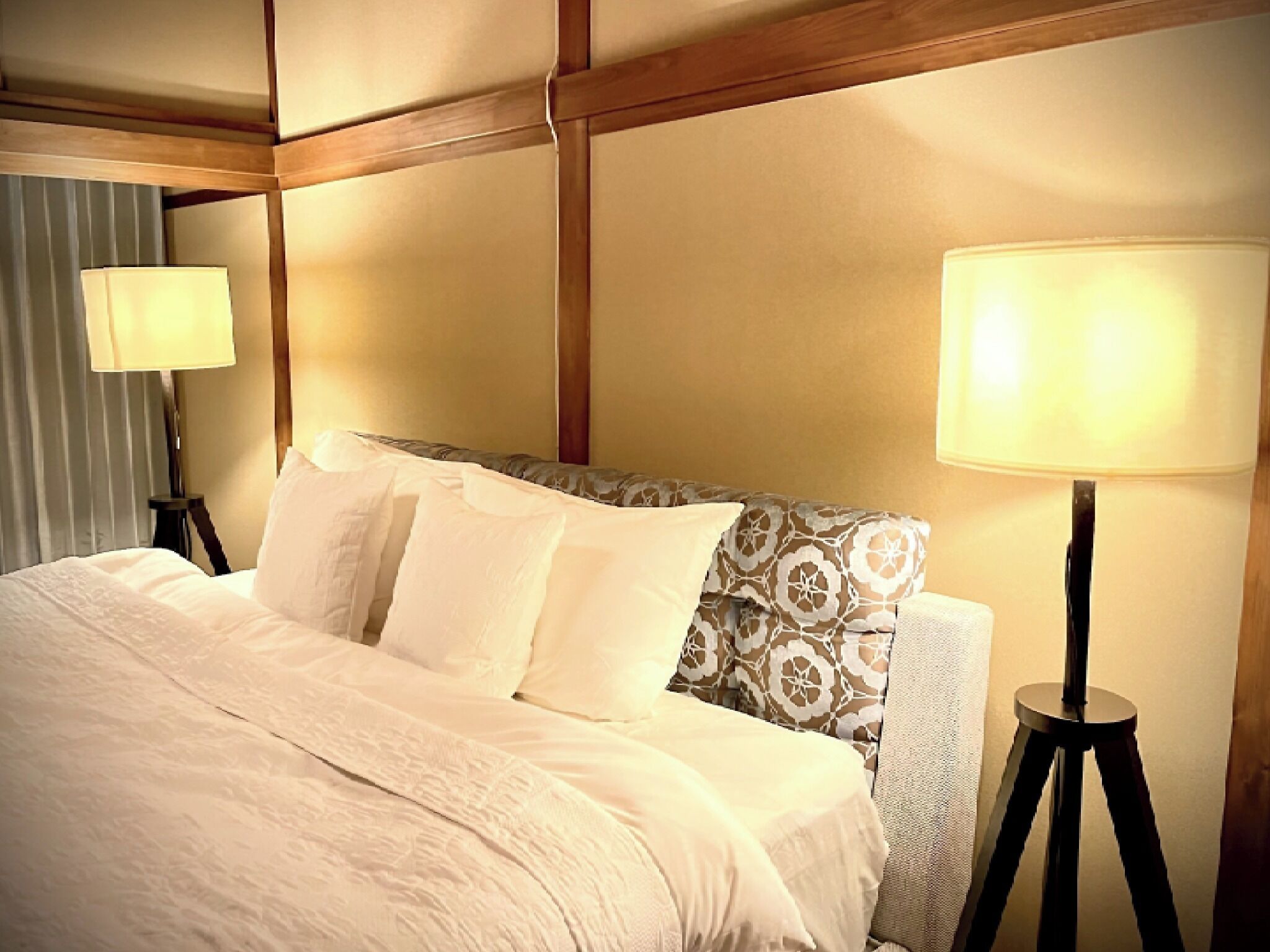 A neatly made bed with white linens, a patterned headboard, and two bedside lamps.