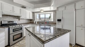 Cocina con gabinetes blancos, encimera de granito, estufa de acero inoxidable y una ventana con una cesta.