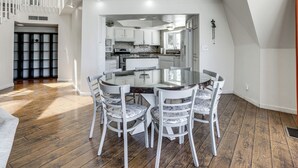 Un comedor con una mesa de vidrio y sillas blancas, una cocina con armarios blancos y una escalera.