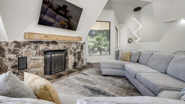 Una sala de estar moderna con chimenea de piedra, un televisor de pantalla plana grande, un sofá seccional gris y un tapete estampado.