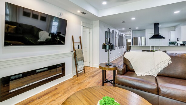A modern living room with a fireplace, a large flat-screen TV, a brown leather sofa, and a wooden coffee table. - Gateway to FSU & FAMU! Family-Friendly Retreat (Tallahassee)