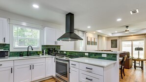 A modern kitchen with white cabinets, a central island, a stove, and a black range hood. - Gateway to FSU & FAMU! Family-Friendly Retreat (Tallahassee)
