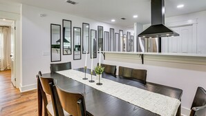 A dining area with a long table, chairs, a central candle holder, and a modern range hood above. - Gateway to FSU & FAMU! Family-Friendly Retreat (Tallahassee)
