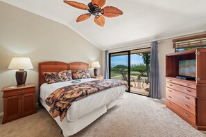 Ein Schlafzimmer mit Bett, Nachttischen, einem Fernsehschrank, einem Deckenventilator und Blick ins Freie.