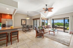 A spacious living area with a large window, a ceiling fan, and a dining area with chairs and a table. - Golf Course Condo Near Beaches & Sunset Views -Kapalua Golf Villas 17P78 (Lahaina)