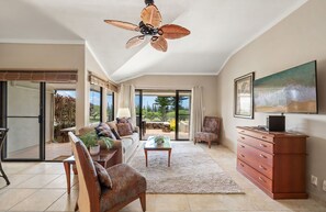 Ein geräumiges Wohnzimmer mit Deckenventilator, einer Couch, einem Couchtisch, einem Fernseher und einem Gemälde.