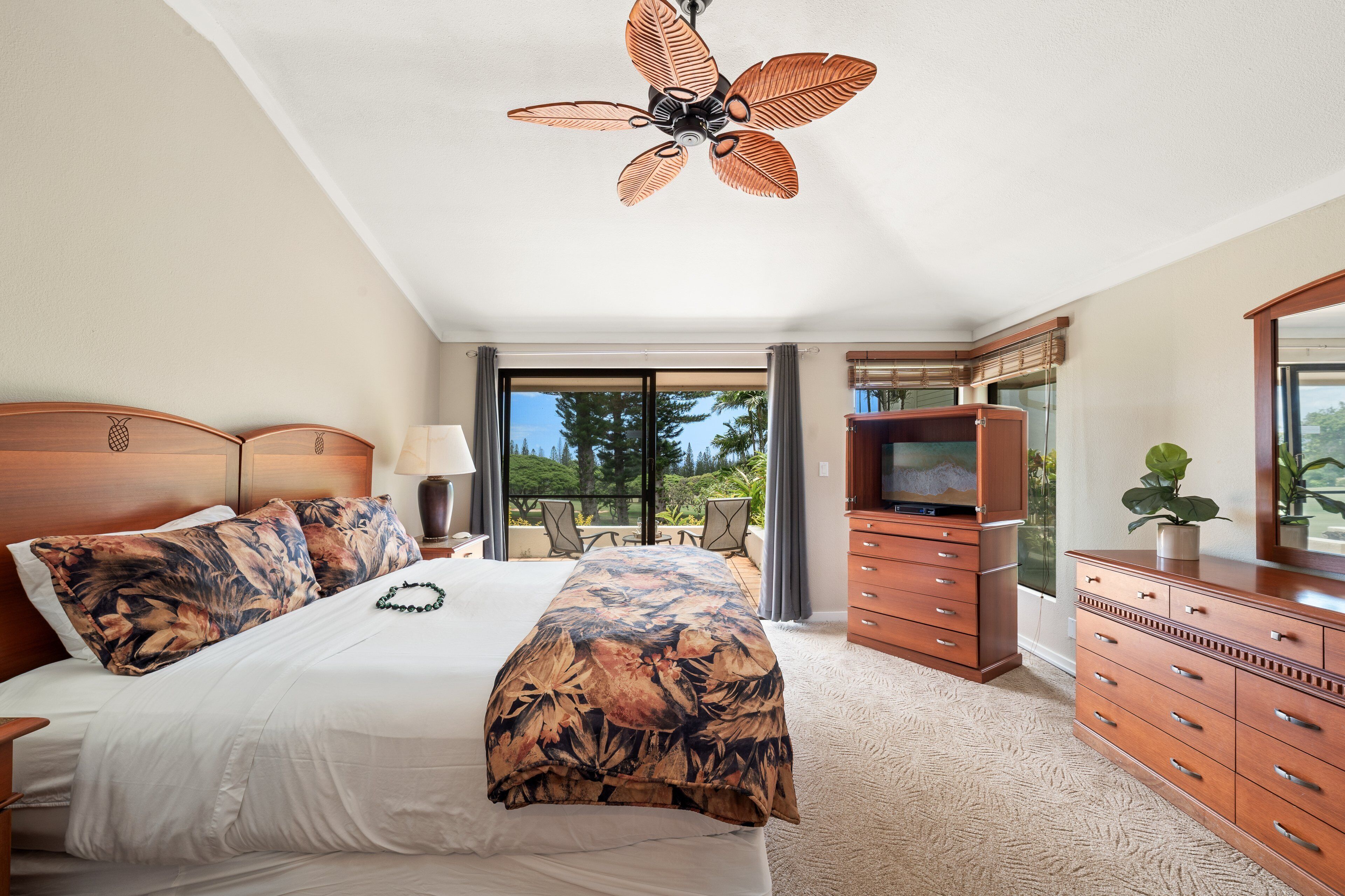 Un dormitorio con cama, ventilador de techo, cómoda, televisor y vistas al exterior.