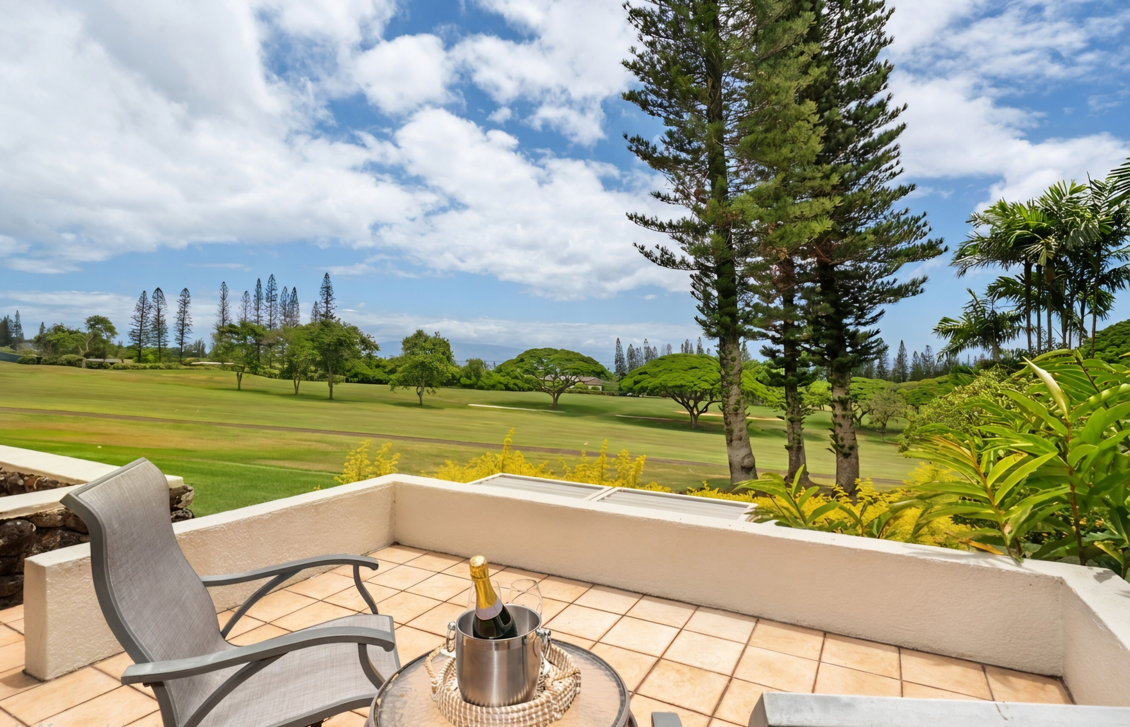 Eine Terrasse mit einem Stuhl, einer Champagnerflasche und Blick auf einen Golfplatz.