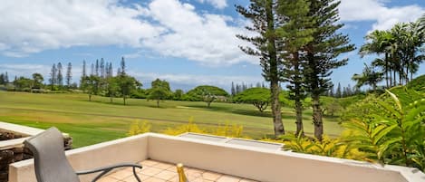 Eine Terrasse mit einem Stuhl, einer Champagnerflasche und Blick auf einen Golfplatz.
