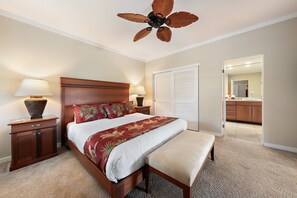 Ein Schlafzimmer mit einem Bett, Nachttischen, einer Bank, einem Deckenventilator und einer Tür zu einem Badezimmer.