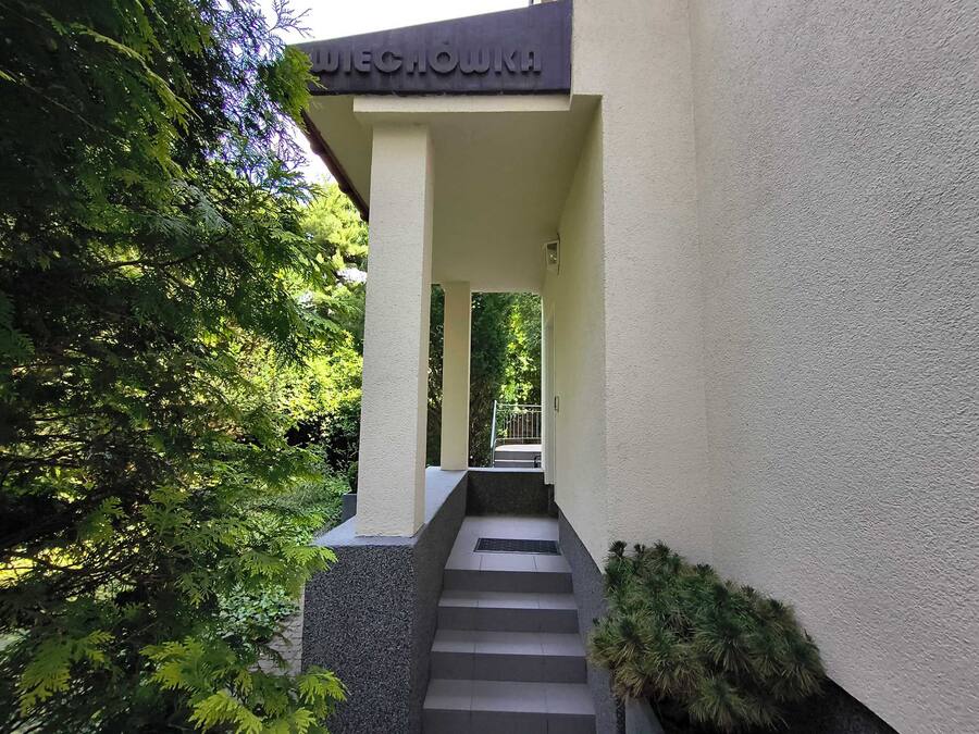 Entrada de un edificio con un letrero que dice 'WECHOWKA', un conjunto de escalones y vegetación circundante.