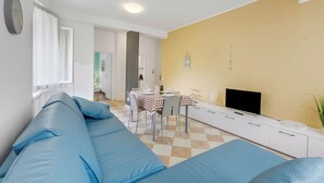 Een woonkamer met een bank, een eettafel met stoelen, een flatscreentelevisie en een gele wand.