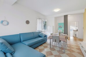 A living room with a blue sofa, a dining table with a checkered tablecloth, and a kitchen area in the background. - Blu Gem Modern (Riva del Garda)