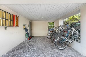 A covered outdoor area with a stone floor, bicycles, and a scooter. - Blu Gem Modern (Riva del Garda)