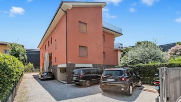 Un immeuble résidentiel à plusieurs étages, doté d’une façade rouge, d’une allée d’accès fermée par un portail et d’un VUS garé.
