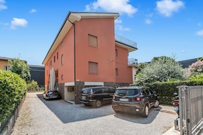 Un edificio residencial de varios pisos con fachada roja, un camino de entrada con portón y un SUV estacionado.