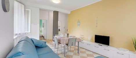 A living room with a sofa, a dining table with chairs, a flat-screen TV, and a yellow wall.