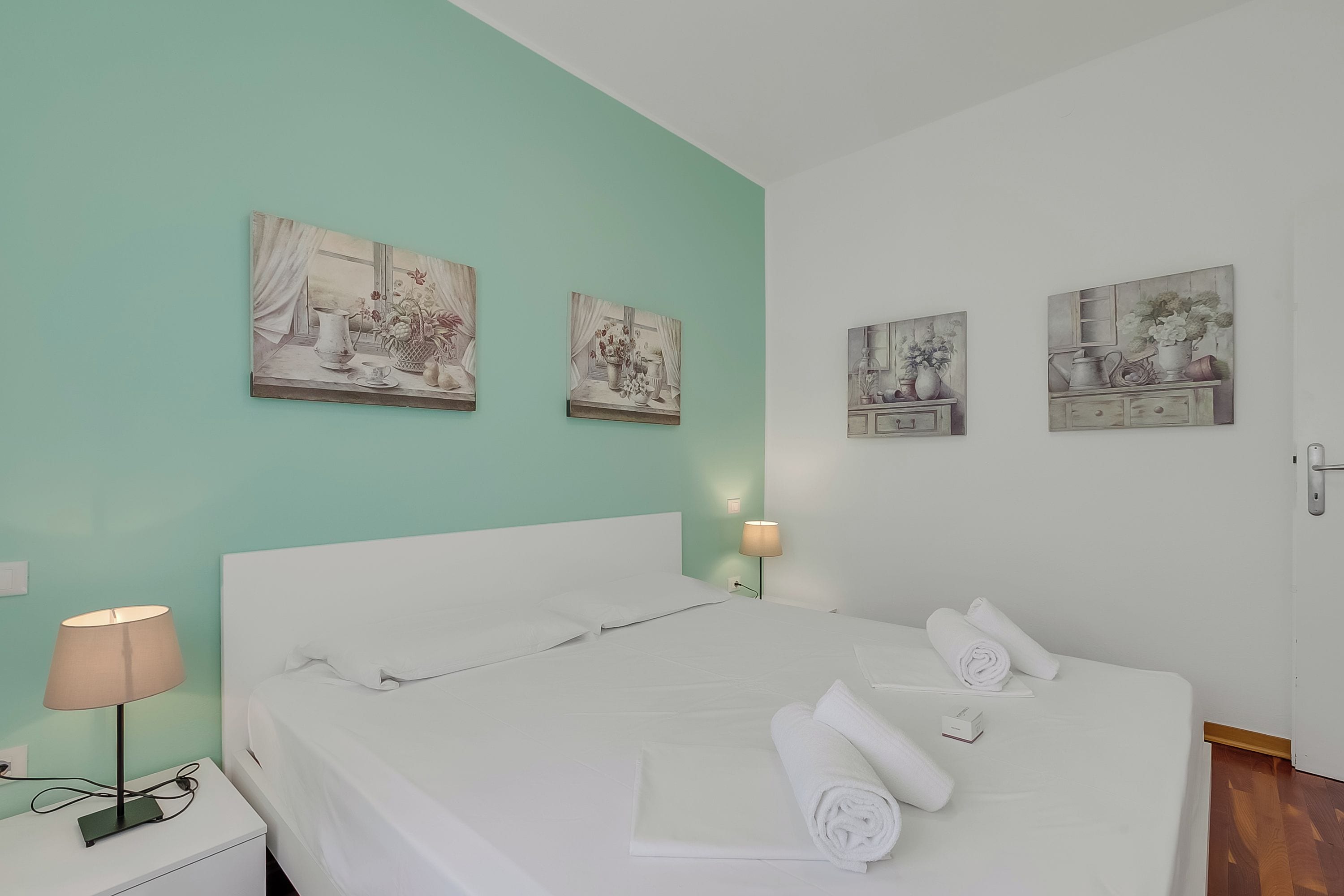 A hotel room with a bed, a nightstand, a lamp, and wall art.