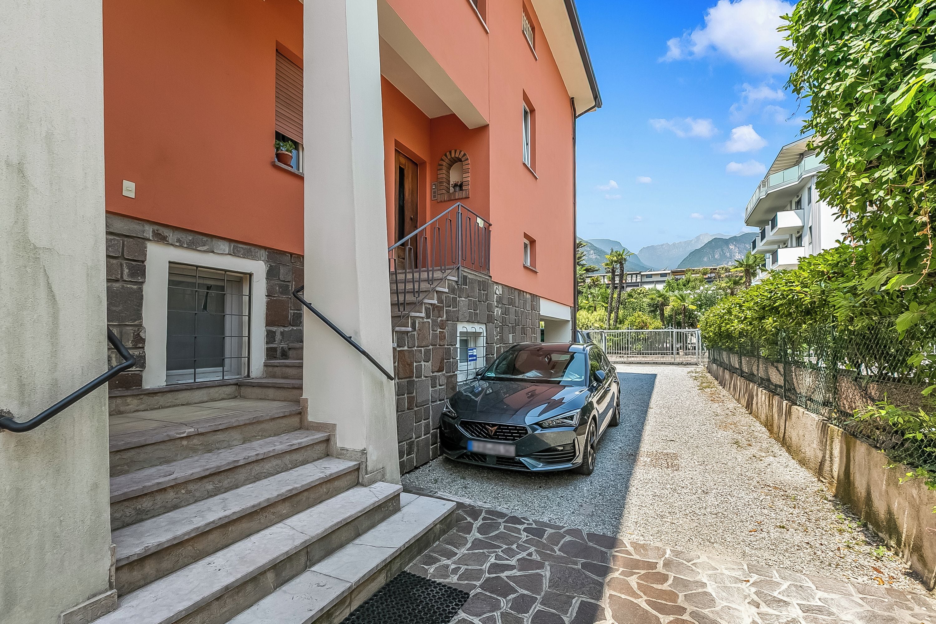 A building with a stone staircase leading to a door, a parked car, and a view of mountains in the background.