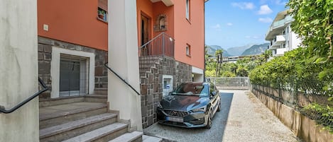 A building with a stone staircase leading to a door, a parked car, and a view of mountains in the background.