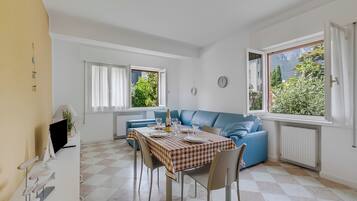 Ein Essbereich mit einem Tisch für vier Personen, einem blauen Sofa und Blick auf Grünflächen.