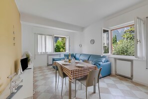 A dining area with a table set for four, a blue sofa, and a view of greenery outside. - Blu Gem Modern (Riva del Garda)