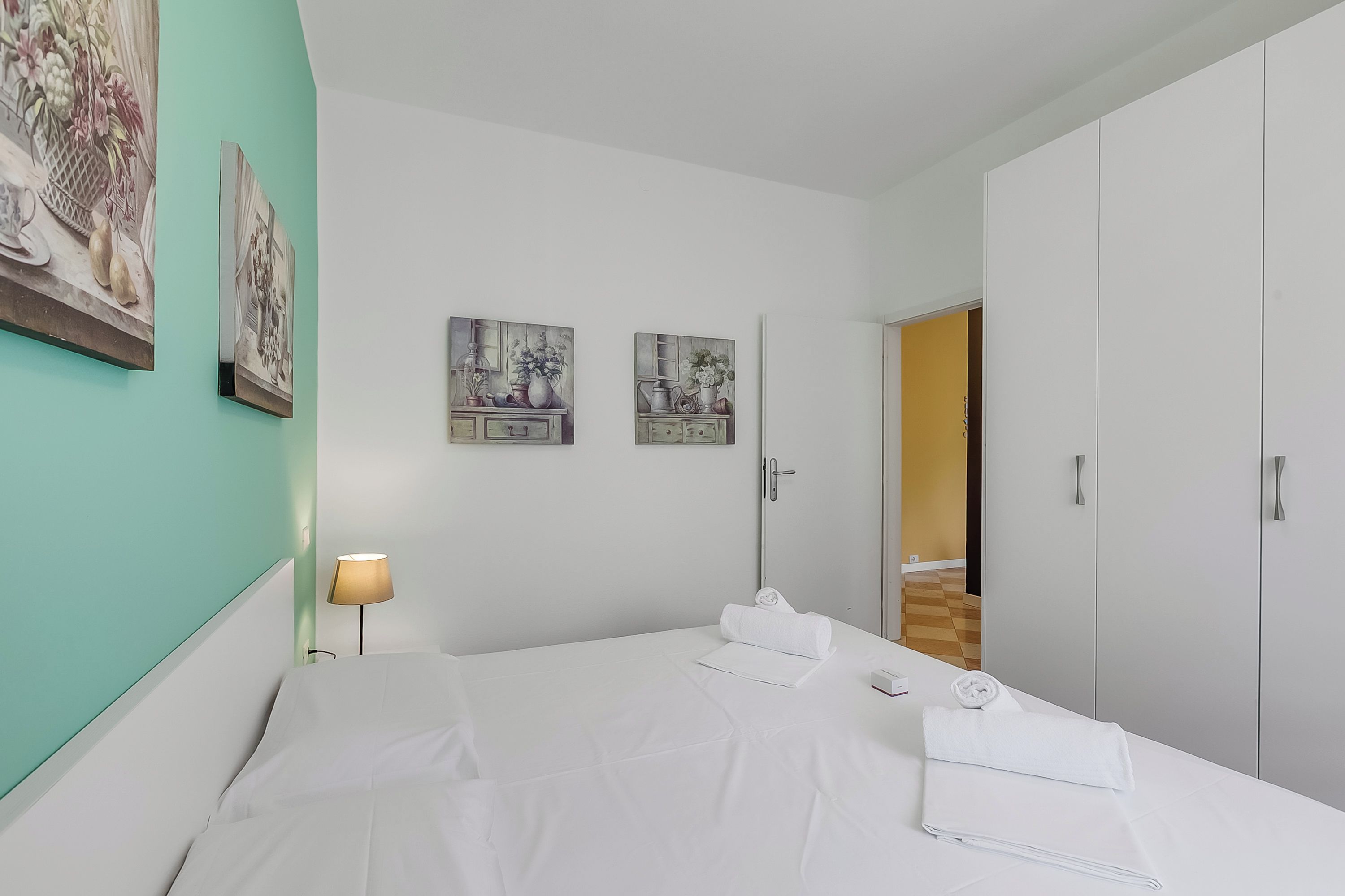 A hotel room with a bed, a nightstand, a lamp, and artwork on the walls.