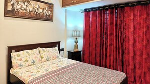 Ein Schlafzimmer mit einem Bett, einem hölzernen Kleiderschrank, einer blumigen Tagesdecke und einem roten Vorhang.