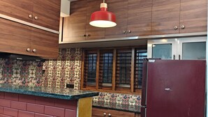 Eine Küche mit Holdekor-Schränken, einer gemusterten Spritzschutzleiste, einem roten Kühlschrank und hängenden Pendelleuchten.