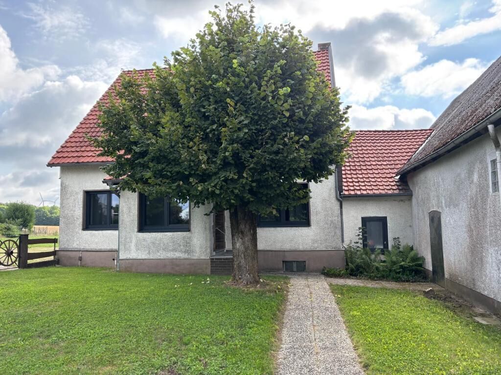 A house with a red-tiled roof, a tree in front, and a gravel path leading to the entrance.