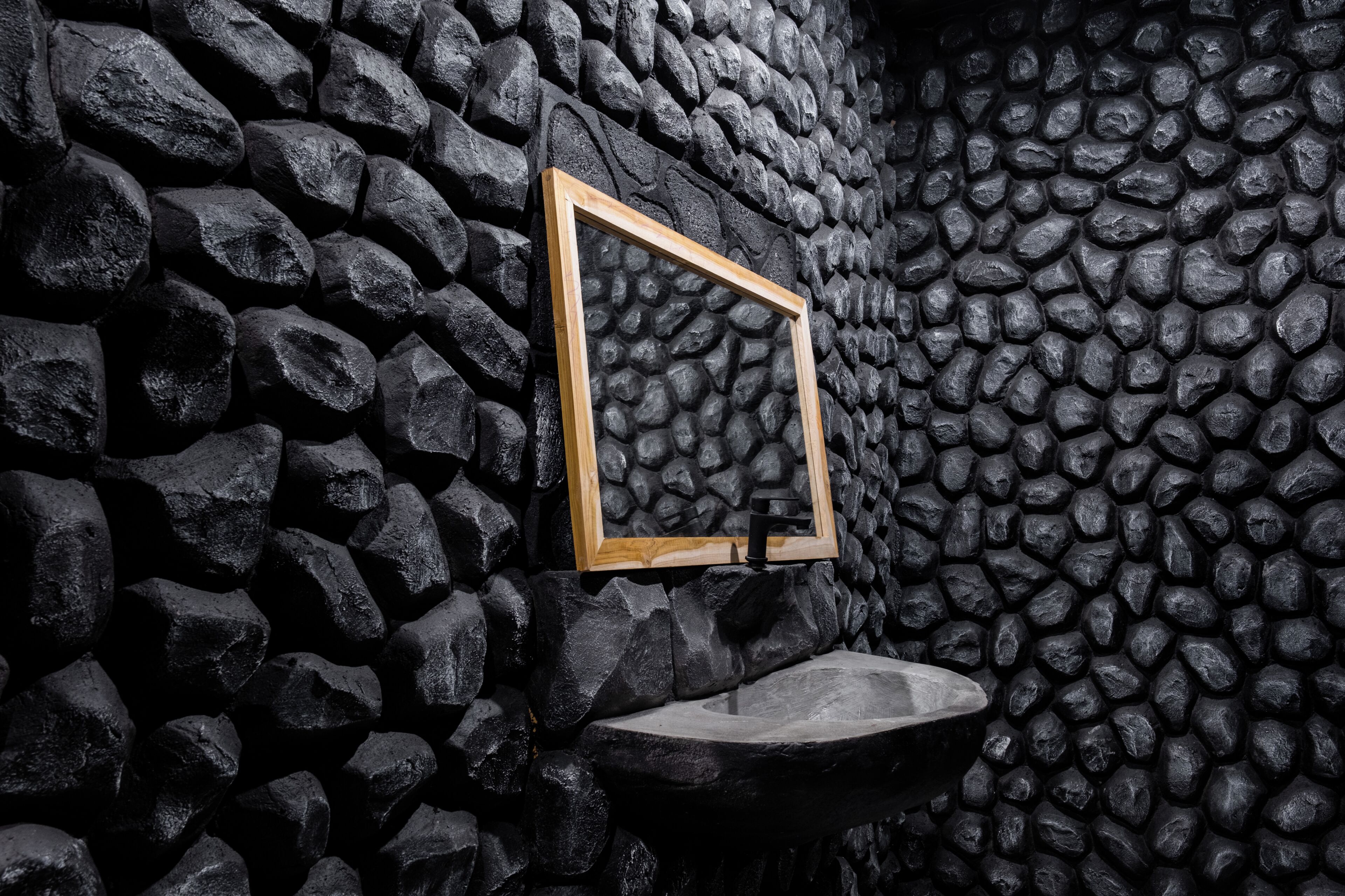 Pared de piedra con espejo de marco de madera y un lavamanos.