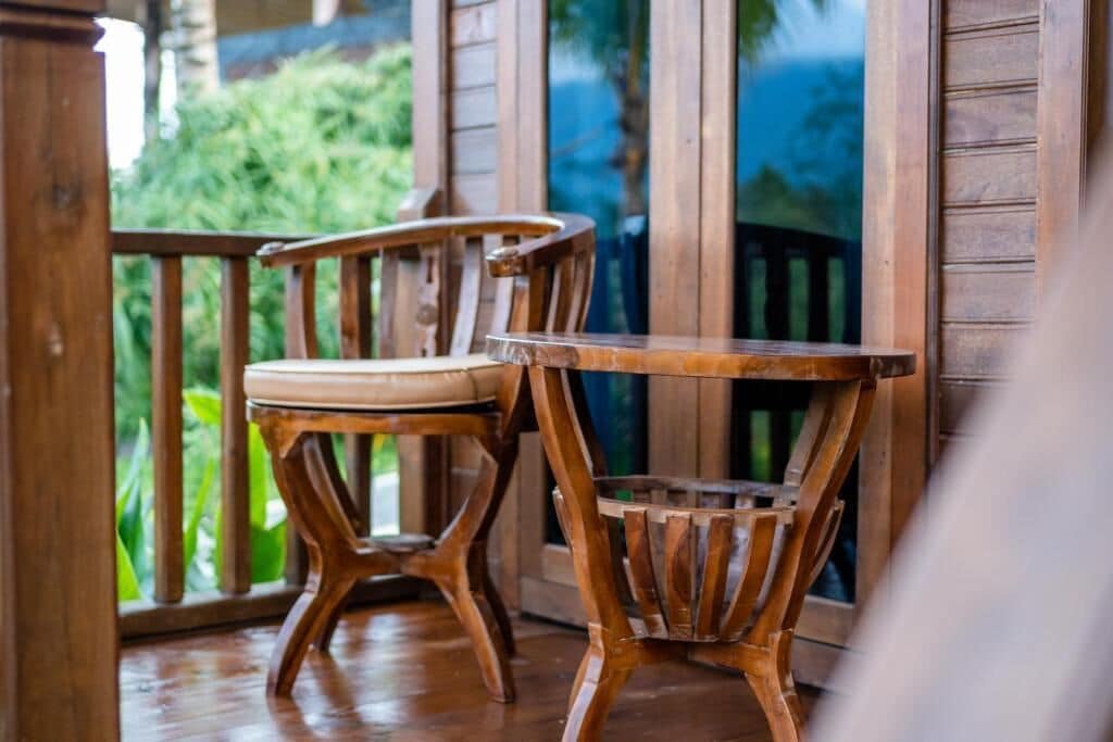 A wooden chair and table on a porch with a view of greenery.