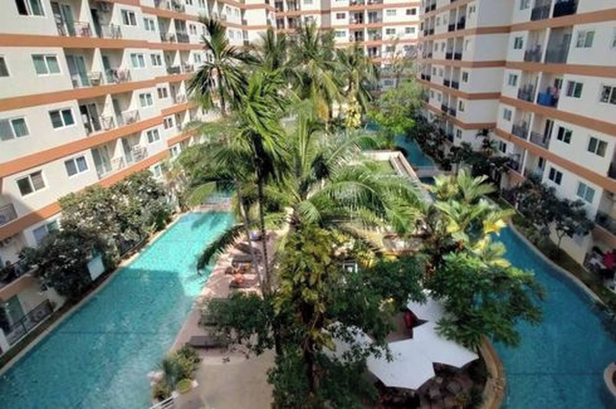 Un hotel de varios pisos con una piscina central rodeada de exuberante vegetación y palmeras.