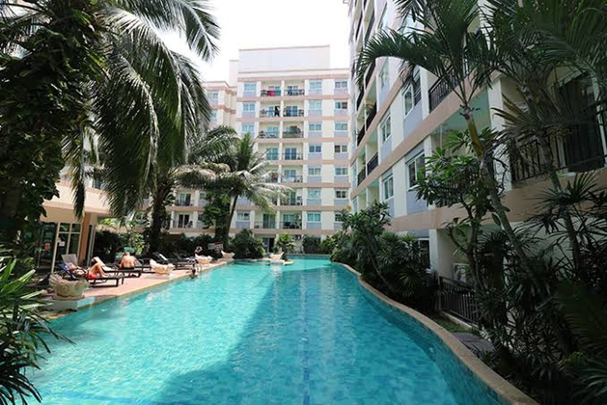 A swimming pool surrounded by palm trees and a multi-story building with balconies.