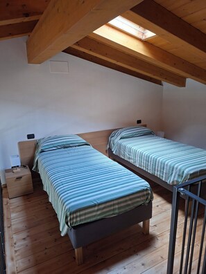 A small, single-room accommodation with two beds, a skylight, wooden flooring, and a simple bedside table with a lamp. - Casa Manerba, near Romantica Beach (Lombardia)